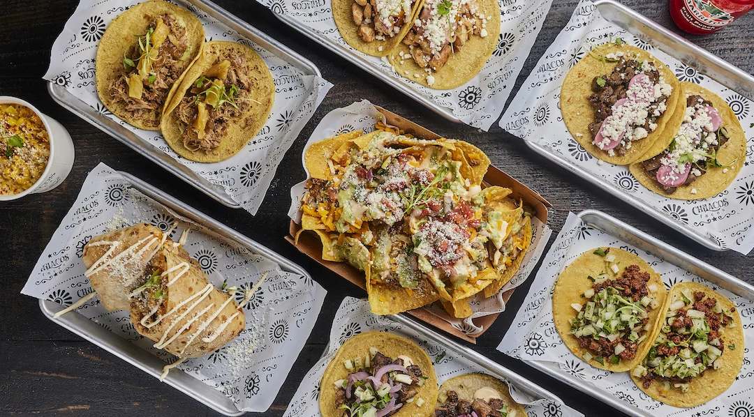 A table of Chilacos tacos, a burrito, loaded nachos and elote